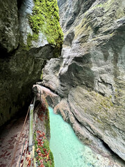A narrow walkway winds through the rock cliffs at the valley's base alongside a flowing stream at Partnachklamm Gorge, Garmisch-Partenkirchen, offering a stunning alpine experience.
