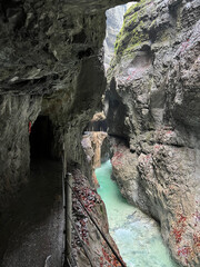 A narrow walkway winds through the rock cliffs at the valley's base alongside a flowing stream at Partnachklamm Gorge, Garmisch-Partenkirchen, offering a stunning alpine experience.