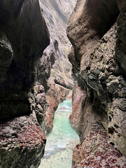 The beautiful stream flows through the rocky valley of Partnachklamm Gorge, where lush moss clings to stones, creating a vibrant and serene natural scene in Garmisch-Partenkirchen.
