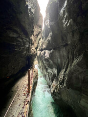 A narrow walkway winds through Partnachklamm Gorge alongside the flowing stream at the valley's base, nestled between dramatic cliffs and lush greenery in Garmisch-Partenkirchen.