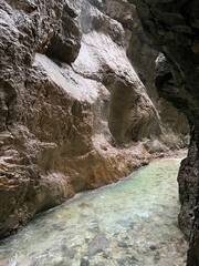 The beautiful stream flows through the rocky valley of Partnachklamm Gorge, where lush moss clings to stones, creating a vibrant and serene natural scene in Garmisch-Partenkirchen.