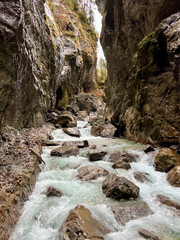 A powerful stream flows through the rocky riverbed of Partnachklamm Gorge, winding between towering cliffs and creating a dramatic, rugged valley scene in the Bavarian Alps.