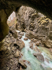 A powerful stream flows through the rocky riverbed of Partnachklamm Gorge, winding between towering cliffs and creating a dramatic, rugged valley scene in the Bavarian Alps.