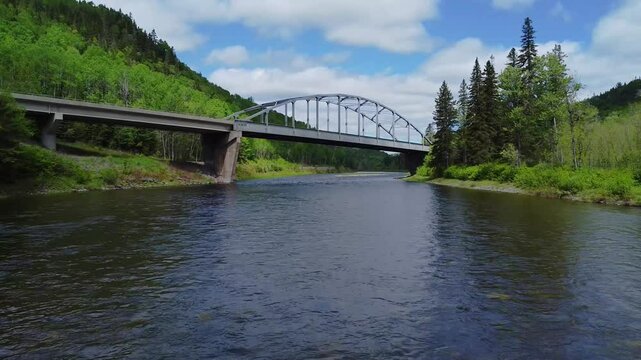 Drone FPV Flight Over Matapedia River Forest passing Under Metal Arch Bridge, Quebec Canada; Aerial Low Altitude Salmon Stream Scenery, Blue Sky and Clouds, Summer Wilderness Landscape