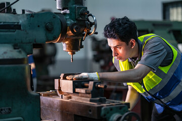 An industrial technician operates a drill press machine with focused precision in a workshop. Wearing safety gloves and a reflective vest, he demonstrates skill and attention to detail on metalwork.