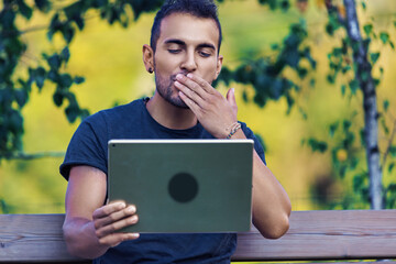 Young man sending a kiss during a video call on tablet in park