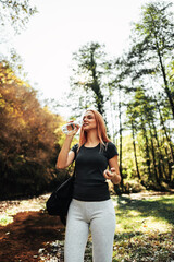 Beautiful young redhead woman walking and jogging in the woods with bottle of drinking water....