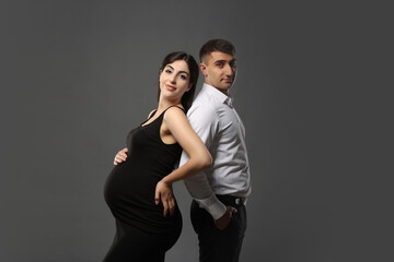 Beautiful pregnant woman with her husband on grey background