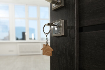 Open door with key and house shaped keychain, closeup. Space for text