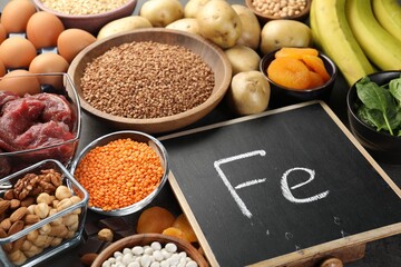 Diet plan for anemia. Different products rich in iron and small chalkboard with Ferrum symbol on table, closeup