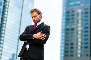 Businessman looking down crossing arms in front of buildings