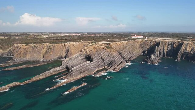 Lighthouse Farol do Cabo Sard&atilde;o at the edge of the steep rock in Portugal. Layers of flysh rock formation are beneath