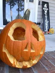 An orange, carved pumpkin on a front porch.
