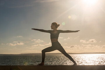 Silhoutte of a sporty woman doing a warrior two yoga pose by the sea