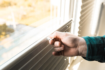 Man installs gray blackout roller blinds on window indoors, closeup.