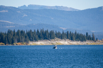 Fototapeta premium a small fishing boat in a dark blue water lake, forest and mountain backdrop