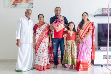 Obraz premium An Indian family wearing traditional and casual costumes spends time with their baby, girl and grandparents in a high-rise apartment building in Kuala Lumpur, Malaysia. June 2024