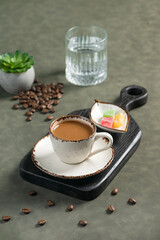 Turkish Coffee: A cup of Turkish coffee served on a black board with a glass of water and Turkish delight. Scattered coffee beans and a small succulent plant are in the background.