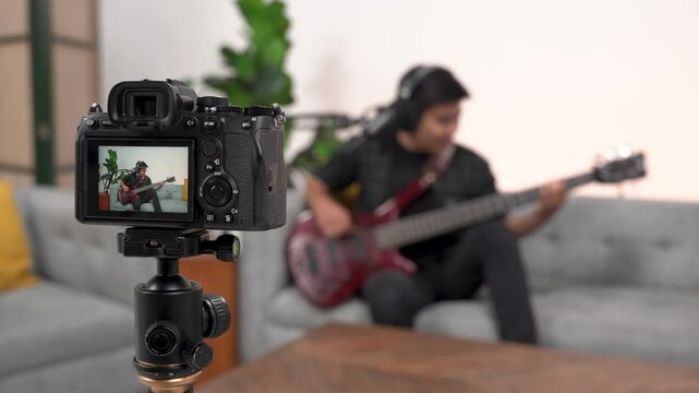 Bassist or guitarist blogger. Asian influencer playing bass, recording music videos using a professional camera on a tripod. Bassist creates video lessons and tutorials for internet vlog classes.