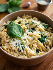 Takeaway food - orzo noodles in cream sauce with spinach in takeaway box on wooden table
