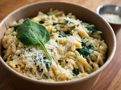 Takeaway food - orzo noodles in cream sauce with spinach in takeaway box on wooden table
