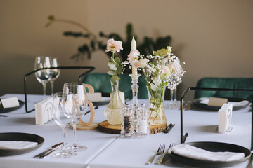 Pastel flowers in glass vases placed on wooden stands. Romantic table decor with flowers and candles for special occasions. Merry decor