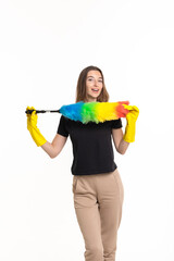 The young woman, dressed in a casual black shirt and beige pants, joyfully demonstrates a colorful feather duster, showcasing her cleaning spirit in a bright setting.