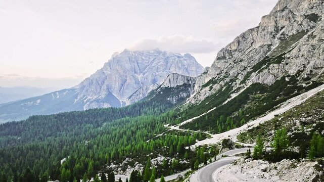 plan au drone route qui traverse les montagnes des alpes itliennes ( Dolomites) au coucher de soleil avec des couleur orang&eacute;e et un ciel bleu le tout entour&eacute; de montagnes majestueuses