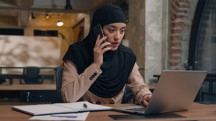 Muslim woman in hijab female office manager businesswoman consult client talk mobile phone at business company Arabian islamic girl freelancer student working with laptop computer write notes at cafe