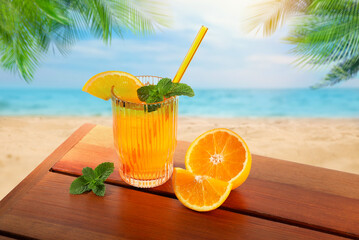 Refreshing drink with straw and fresh orange on wooden table at beach