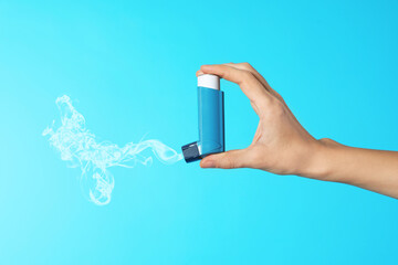 Asthma treatment. Woman holding inhaler on light blue background, closeup. Aerosolized medication...