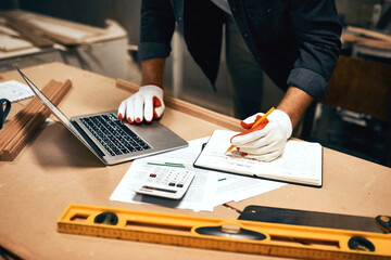 Carpenter, laptop and hands with notebook for construction, furniture or project notes. Handyman,...