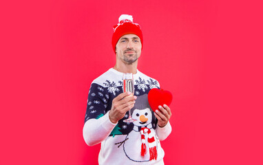 smiling man in christmas hat with champagne and heart. christmas man isolated on red background.