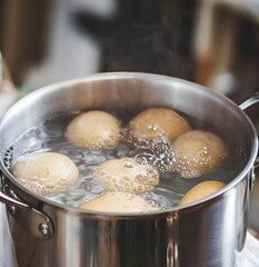 A photo of a boiling pot of water with a few small potatoes inside. The pot is placed on a wooden table, and there's a white cloth on the table. The background is blurred and contains other objects.