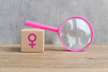 Menopause concept..Pink magnifying glass over a wooden cube with a women symbol on wooden table.