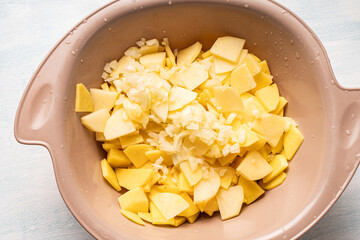 Raw chopped potatoes and finely chopped onions in a bowl. Top view, close-up.