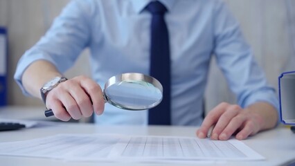 Businessman is carefully examining financial documents with a magnifying glass, highlighting the importance of thorough analysis in business. Audit and taxes