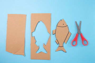 A layout of fish cut out from cardboard, materials and scissors on a blue background, showcasing a...