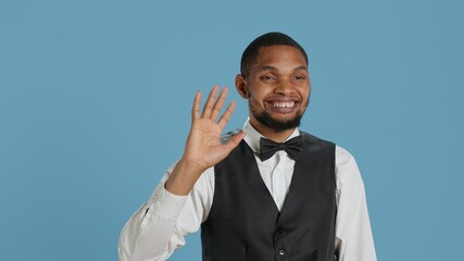 Bellboy employee smiling and waving hello at hotel guests, greeting people with confidence and offering luxury services for a pleasant stay. Cheerful personnel saying hi to people. Camera A.