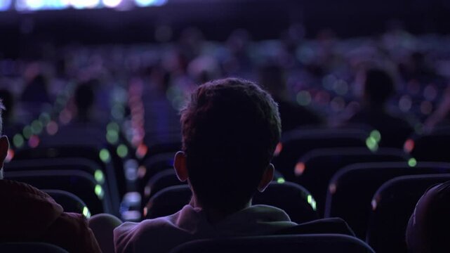 A movie theater full with diverse audience watching an exciting movie back view