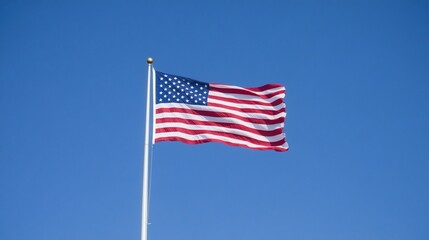 Fototapeta premium American flag waving in the wind against a blue sky.