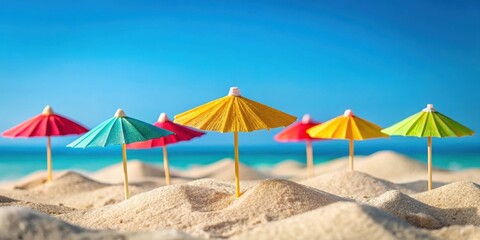 Fototapeta premium A row of colorful miniature umbrellas planted in the sand on a sunny beach with a blue sky and turquoise ocean in the background.