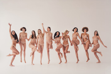 Obraz premium Studio no retouch photo of adorable cute ladies dressed lingerie enjoying girls power jumping holding arms isolated beige color wall background