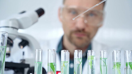 Man researcher with safety glasses is working with lab tubes using a pipette in laboratory, close-up of lab equipment. Science and medicine