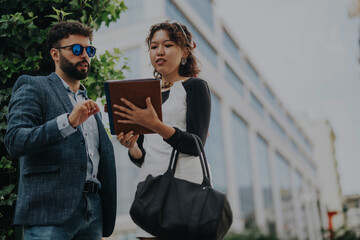 Diverse business people engage in a collaborative meeting outdoors, discussing strategies and analyzing projects in a modern urban setting for sales and revenue growth.
