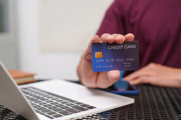 cheerful businessman sits at his desk, using a laptop to make an online purchase. With a credit card in hand, he connects to e-commerce, enjoying seamless technology and finance solutions.
