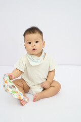 Fototapeta premium A Baby Sitting on the Floor Floor with natural white background and playing with a towel