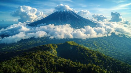 Fototapeta premium A majestic snow-capped volcano rises above a lush green mountain range, with clouds swirling around its peak.