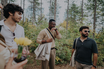 A diverse group of friends enjoys a relaxing walk in a lush forest setting, engaging in friendly conversation and carrying backpacks. The tranquil environment adds to their pleasant outdoor experience