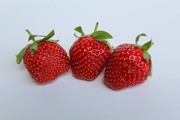 Three red strawberries with green stem, isolated on white background